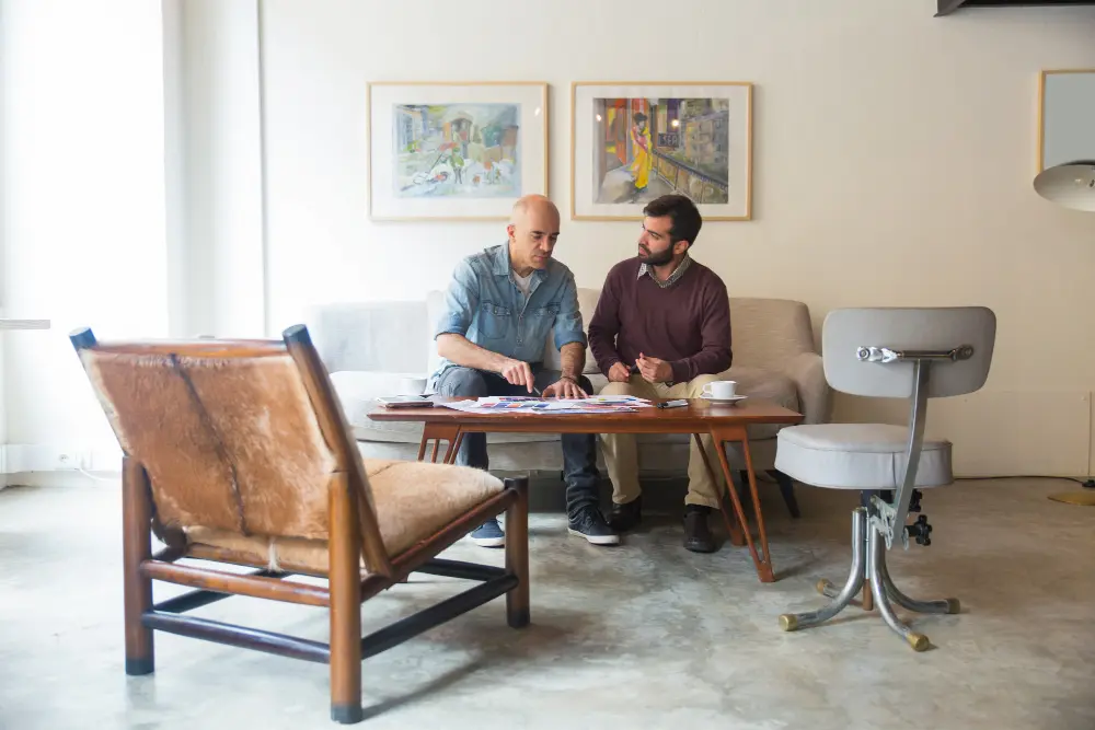 Tailor and client discussing suit options in a comfortable home setting.