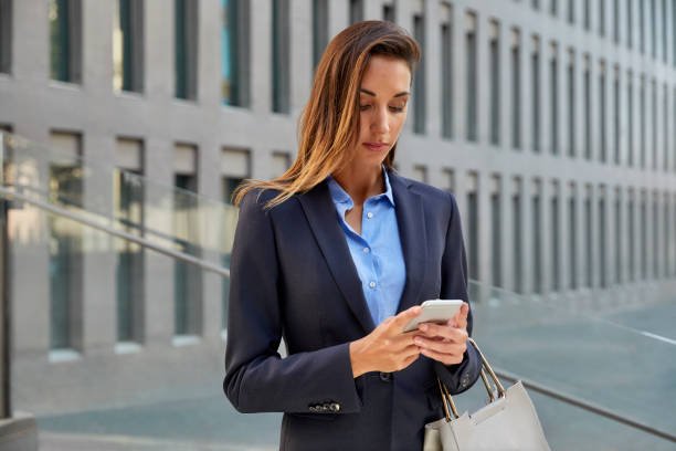 Young businesswoman texting on smart phone against office. Beautiful professional is wearing suit. Female executive is standing in city.